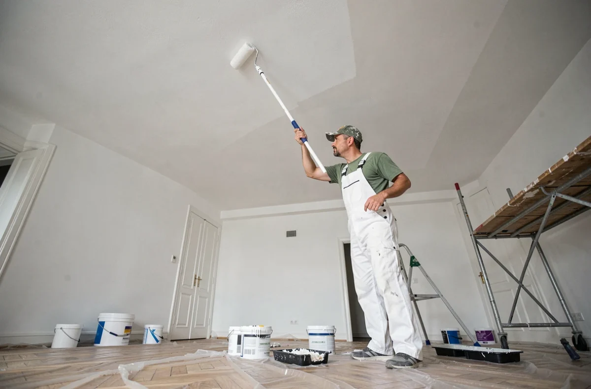 Peintre professionnel appliquant de la peinture blanche de qualité sur un plafond de 50m2 avec un rouleau à manche long dans un appartement parisien